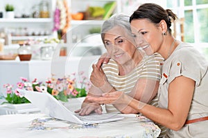 Mother and daughter sitting at table with laptop, at home