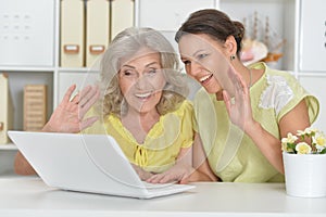 Mother and daughter sitting at table with laptop, at home