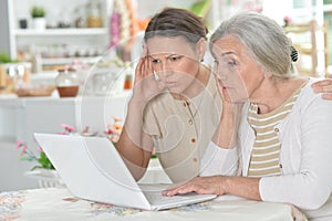 Mother and daughter sitting at table with laptop, at home