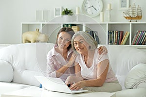 Mother and daughter sitting at table with laptop, at home