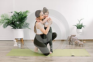 Mother and daughter spending time together doing yoga exercise home. Pretty woman and little child girl, hugging each