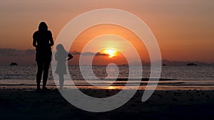 Mother and daughter stand on sunset sea beach