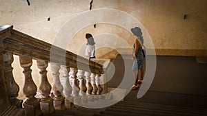 Mother and daughter standing on landing in old building with marble railing leading down to them