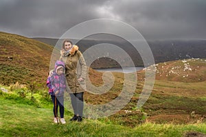 Mother and daughter standing and looking at camera, Lough Bray in background. Wicklow Mountains