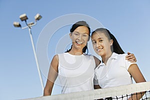 Mother and daughter standing at net on tennis court portrait low angle view