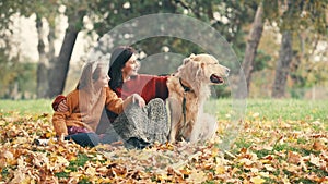Mother and daughter stroking golden rertriever dog in autumn park