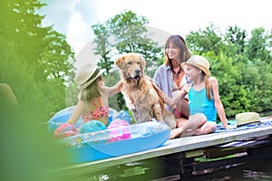 Mother and daughter stroking golden retriever on pier during summer weekend