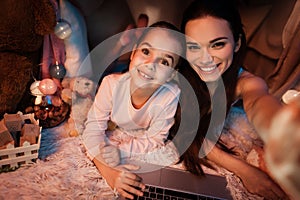 Mother and daughter taking selfie in pillow house late at night at home.