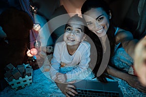 Mother and daughter taking selfie in pillow house late at night at home.