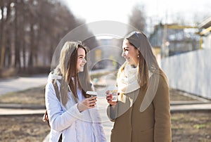 Mother and daughter talking, laughing smiling on the street, drinking coffee in cups