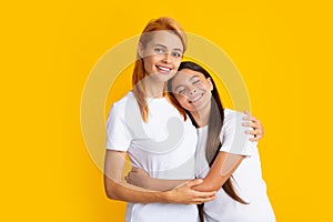 Mother and daughter teenager girl in t-shirt embrace cudding isolated on yellow color background studio. Mothers day