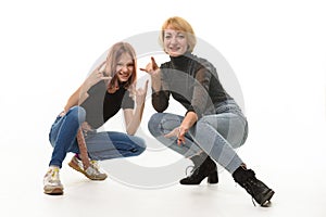 Mother and daughter teenager knelt down and cheerfully show youth gestures in the frame