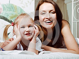 Mother with daughter together in bed smiling, happy family close