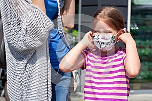 Mother and daughter together, little girl putting on or taking off protective anti viral medical face mask. Family shopping