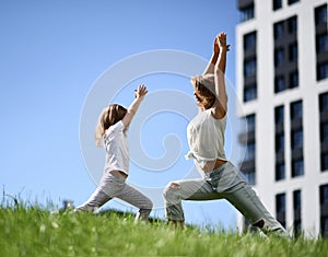 Mother and daughter together practicing yoga outside on a grass together urban city
