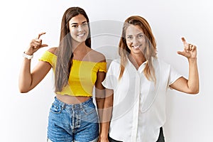 Mother and daughter together standing together over isolated background smiling and confident gesturing with hand doing small size