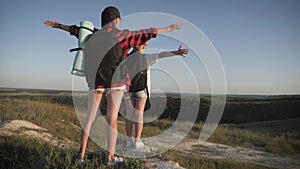 Mother and daughter on top of a mountain. Hikers with backpack standing on cliff and looking to a sky. Family tourism