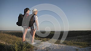 Mother and daughter on top of a mountain. Hikers with backpack standing on cliff and looking to a sky. Family tourism