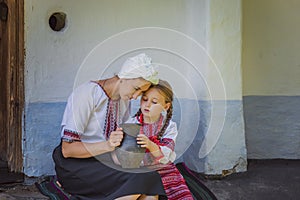 mother and daughter in Ukrainian national costumes are sitting near the house