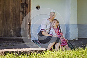 mother and daughter in Ukrainian national costumes are sitting near the house