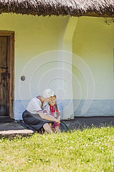 mother and daughter in Ukrainian national costumes are sitting near the house