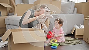 Mother and daughter unpacking teddy bear of cardboard box playing on floor at new home