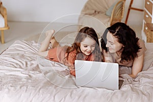 Mother and daughter using laptop on bed in holiday at home.