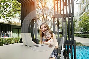Mother and daughter use laptop for online shopping on background of swimming pool on sunny day