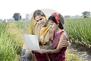Mother with daughter using laptop on agriculture field