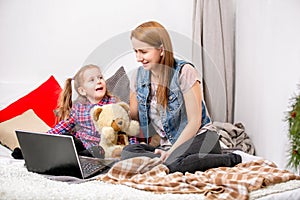 Mother and daughter using laptop on bed in bedroom. They look at the display and laugh.