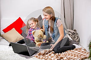 Mother and daughter using laptop on bed in bedroom. They look at the display and laugh.