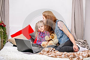 Mother and daughter using laptop on bed in bedroom. Mother hugging and kissing daughter