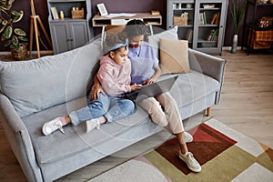 mother and daughter using laptop together sitting on sofa in cozy home