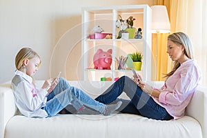 Mother and daughter using phones while sitting on sofa. Smartphone  addiction concept