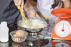 Mother and daughter using whisk to mix egg and wheat flour