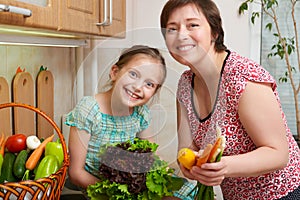 Mother and daughter with vegetables and fresh fruits in kitchen interior. Parent and child. Healthy food concept