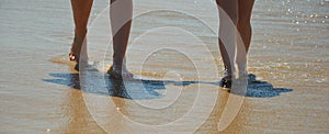 Mother and daughter walk along the seashore. family summer vacation. feet on the water. background for the design.