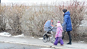 Mother with Daughter Walkin in Park with Newborn Child in Baby Carriage
