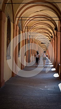 Mother and daughter walking through arched portico in a summer day