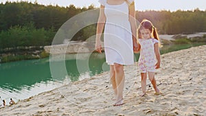 Mother and daughter walking on the beach at the beautiful lake with azure water, my mother is a girl`s arm