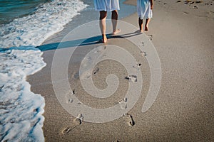 Mother and daughter walking on beach leaving footprint in sand