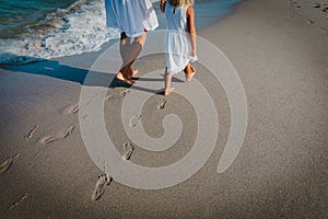 Mother and daughter walking on beach leaving footprint in sand