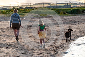 Mother and daughter walking dog along beach in the golden light of the setting sun