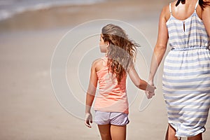 Enjoying a day at the beach with mom. A mother a daughter walking hand in hand on the beach.