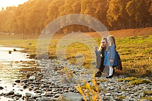 Mother and daughter walking near river in autumn time. Happy family. Fall weekend in the open air. Family enjoying beautiful autum