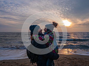 Mother and daughter in warm clothes on empty beach with blue sea sunset sky. South scenic landscape wallpaper