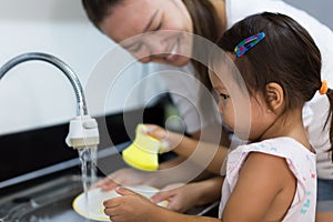 Mother and daughter washing dishes together at home