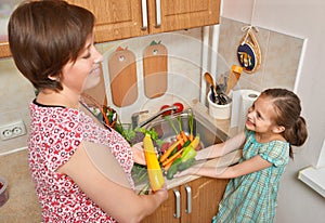 Mother and daughter washing vegetables and fresh fruits in kitchen interior, healthy food concept