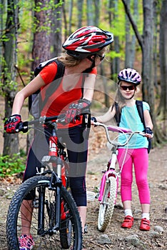 Mother and daughter wearing helmet are cycling on bicycle .
