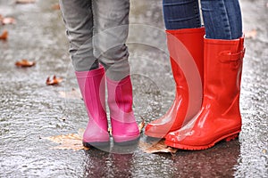 Mother and daughter wearing rubber boots after rain, focus of legs.